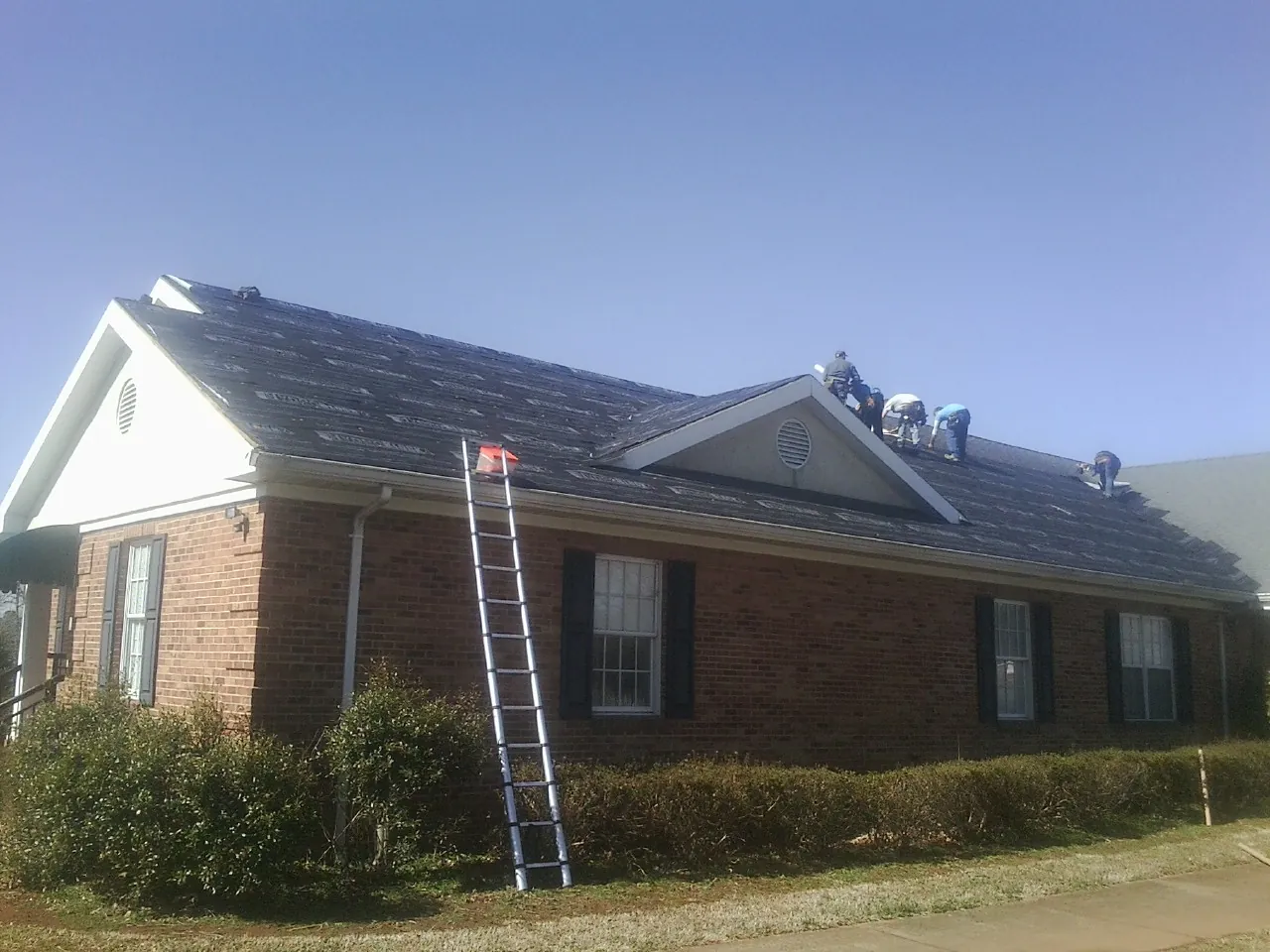 Crew tearing shingles off a brick ranch roof with a ladder set — Emergency Roof Repair work by our crew in Bremen